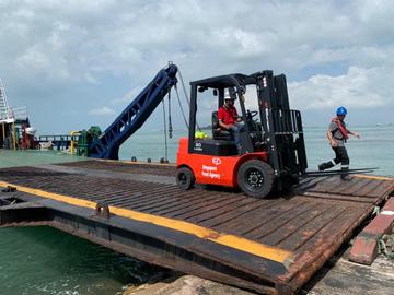 Forklift loading materials on a jetty barge at a waterfront site in Johor