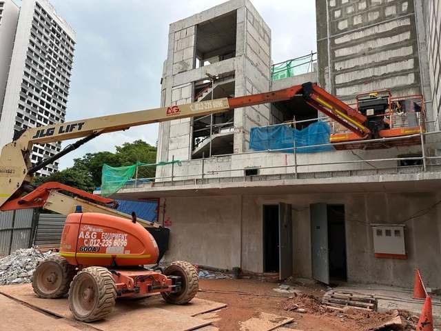 JLG 600AJ articulated boom lift reaching over a ledge on a construction site in Johor