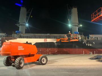 Telescopic boom lift working at night on a port wharf beside a ship in Johor