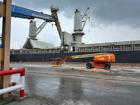 Telescopic boom lift on rental parked on a wharf beside a cargo ship in Johor